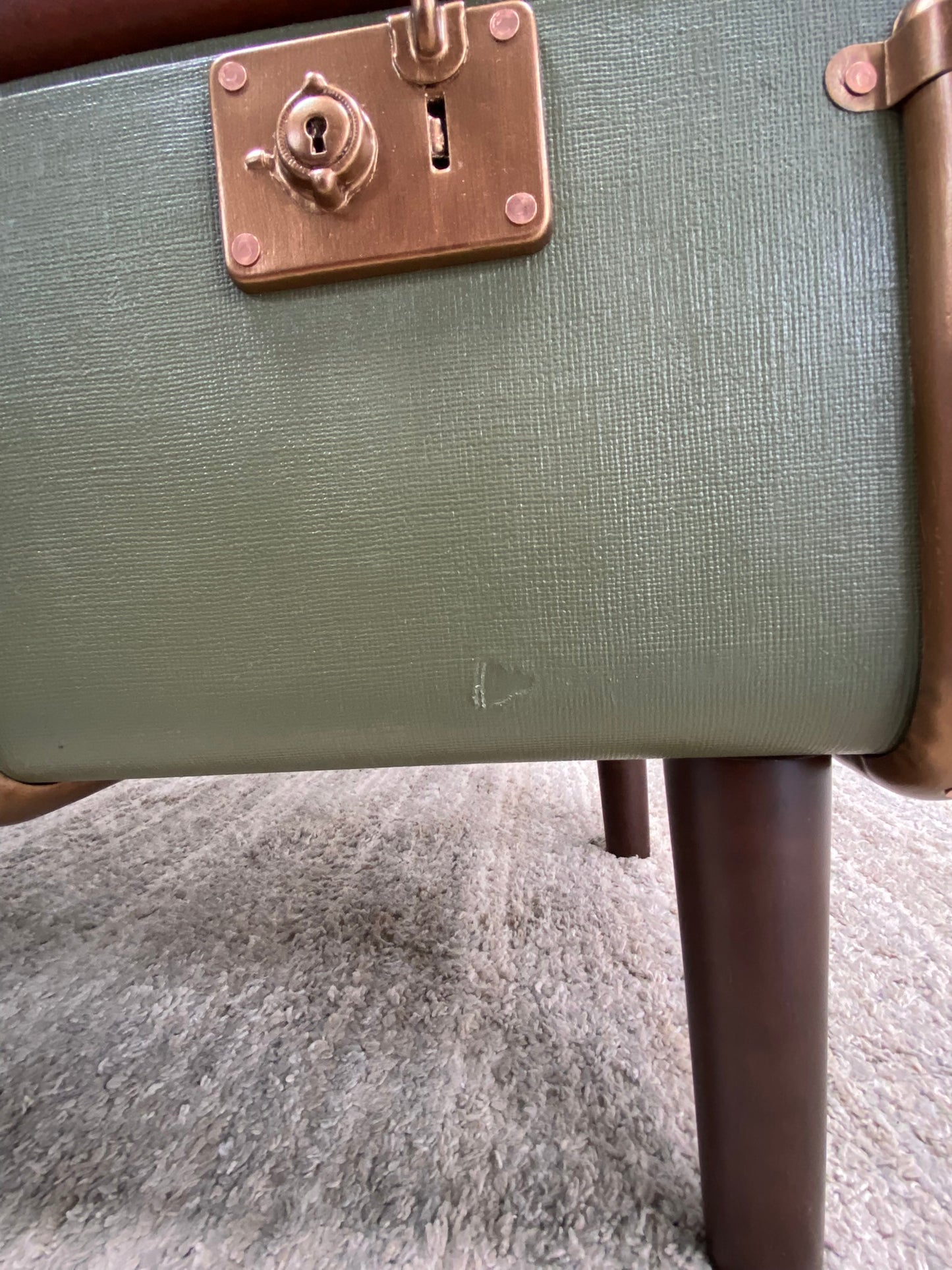 Green suitcase with a brass handle and lock on a textured surface with minor damage