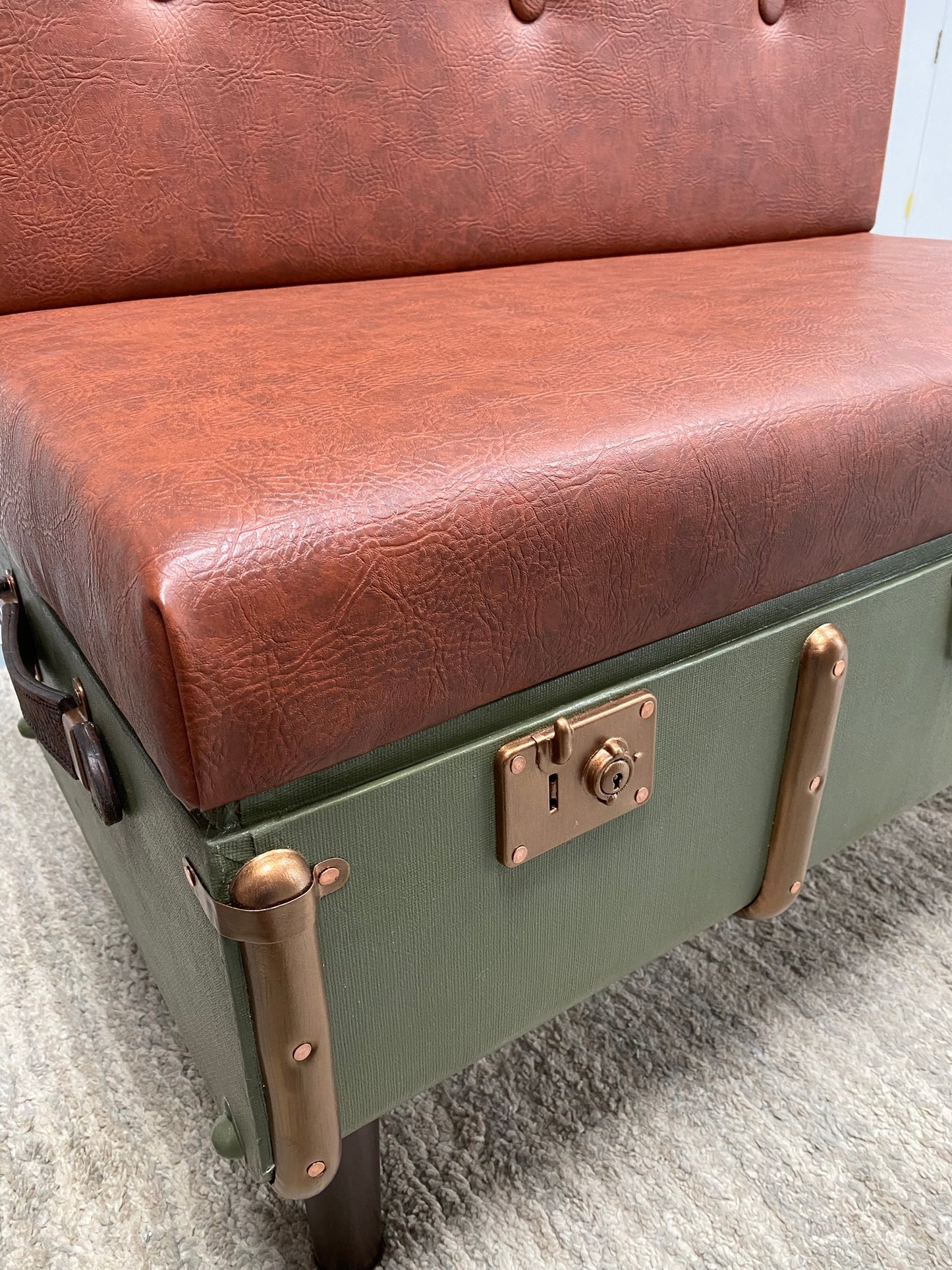 Green suitcase with brown leather seat on a gray carpet