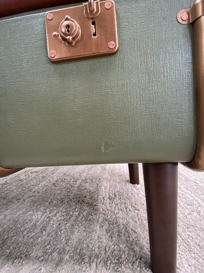 Green suitcase with a brass handle and lock on a textured surface with minor damage